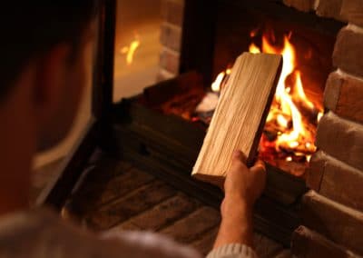 man,putting,dry,firewood,into,fireplace,at,home,,closeup.,winter